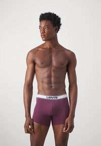 Bordo bokserice z belim pasom z logotipom Levi's. Gladek material, oprijet dizajn in dolžina do sredine stegen.