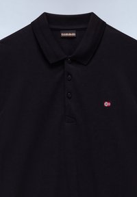 Sort poloshirt med tre knapper, et lille norsk flag broderet på brystet og et synligt mærkelabel indeni kraven.