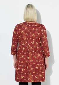 Rotes Blumenkleid mit Dreiviertelärmeln, das gelbe und grüne Blumenmuster aufweist, eine geraffte Taille hat und aus weichem Stoff besteht.