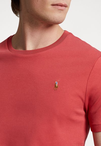 Krátky rukáv tričko vo svetlej červenej farbe z bavlny. S klasickým výstrihom a malým vyšitým logom polo hráča na hrudi. Hladká textúra.