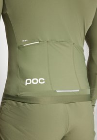 Haut de sport vert olive avec un design ajusté, comportant une bande réfléchissante et un logo "poc" blanc dans le bas du dos. Tissu lisse et extensible.