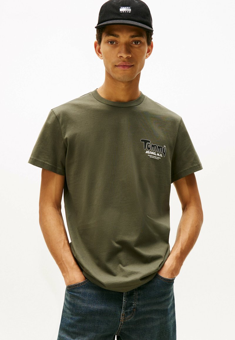 Camiseta de algodón verde oliva con escote redondo y mangas cortas, que presenta el logo "Tommy Jeans, N.Y." en el lado izquierdo del pecho. Diseño casual.