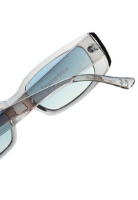 Occhiali da sole con montatura trasparente, lenti blu ombreggiate e dettagli metallici in tonalità argento. Include il marchio sulla parte interna della montatura.