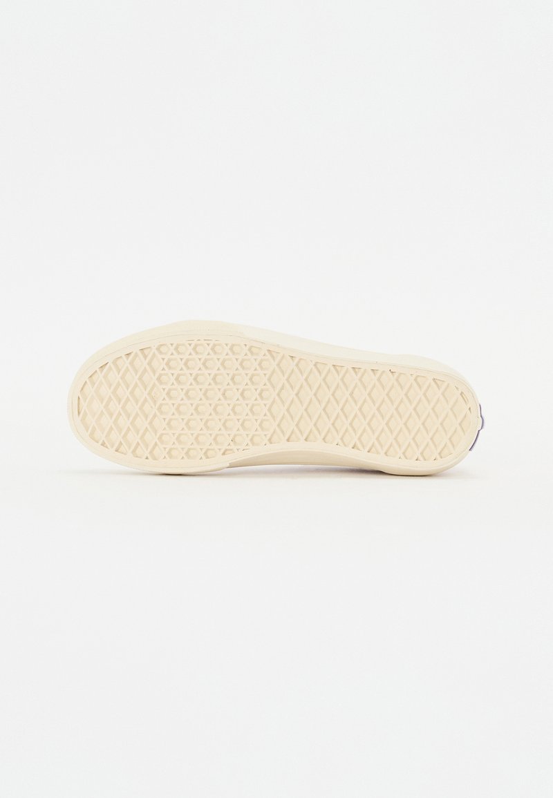 Suela de una zapatilla de goma crema con un patrón de diamante texturizado para mejorar el agarre, y un borde liso. Fondo blanco liso.