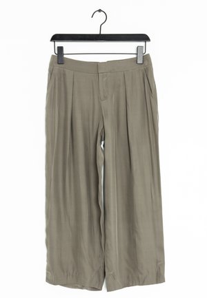 Pantalon kaki à jambes larges avec une texture lisse, présentant des plis à l'avant, une ceinture plate, et une fermeture à crochet, suspendu à un crochet noir.