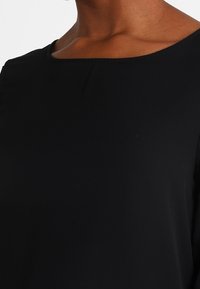 Haut noir à manches courtes avec un col carré, texture lisse et design simple, sans motifs visibles ni détails matériels.