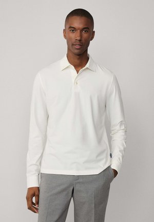 Polo shirt blanc à manches longues avec un col classique et trois boutons ; associé à un pantalon gris sur mesure. Le tissu semble lisse et léger.