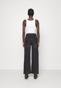 Black wide-leg jeans with five pockets and stitching details, paired with a white sleeveless top and black shoes, viewed from the back.