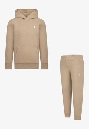 Tannenkleurige hoodie met voorzak en wit logo; gecombineerd met bijpassende aansluitende sweatpants. Beide gemaakt van zacht, gestructureerd materiaal.