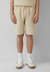 Cremfarbene Shorts aus strukturiertem Stoff mit vertikalen Streifen, ausgestattet mit einem elastischen Bund und einer Kordel. Kombiniert mit weißen Sneakern.