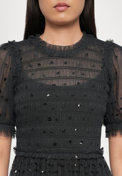 Zwarte jurk van textuurstof met doorschijnende mouwen, versierd met rijen delicate pailletten en een gerimpelde halslijn.
