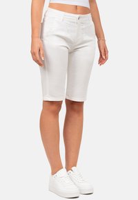 Shorts en denim blanc de type bermuda avec une coupe ajustée, taille mi-haute et détails cousus. Assortis à des baskets blanches pour un look harmonieux.