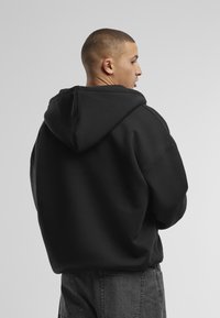 Schwarzer Hoodie aus Baumwollmischung, mit lockerem Schnitt, großer Kapuze und abfallenden Schultern. Schlichtes Design ohne sichtbare Logos oder Muster.