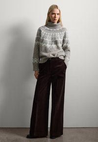 Pull en tricot épais gris avec un col monté, orné de motifs blancs ; associé à un pantalon large en velours côtelé marron foncé.
