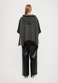 Black and gray poncho with hood, featuring a repeating letter pattern, paired with leather-like black trousers and high-heeled shoes.