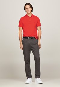 Röd polo skjorta med klassisk krage, i kombination med mörkgrå chinos och vita sneakers. Skjortan har en subtil textur och logodetalj.