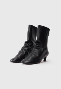 Bottes de cheville en cuir noir avec un design loose, bouts pointus et un petit talon. Texture lisse avec un matériel minimal et sans motifs visibles.