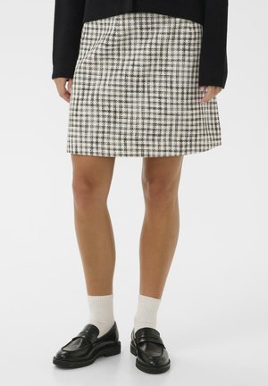 Jupe en mélange de laine à motif écossais noir et blanc, présentant une silhouette droite et des poches latérales, assortie à des mocassins noirs et des chaussettes blanches.