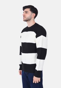 Maglione a righe bianco e nero con un design a maglia testurizzata, caratterizzato da ampie righe orizzontali e polsini a costina, collo a giro.