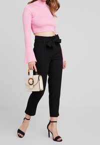 Černé kalhoty s vysokým pasem a mašlí v pase, spárované s růžovým žebrovaným crop topem. Doplněno bílou kabelkou.