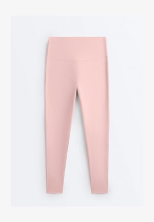 Világos rózsaszín, magasderekú, varrás nélküli leggings, testhezálló szabással, egyszerű világos háttér előtt bemutatva.