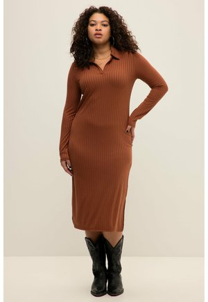 Braunes, geripptes Strickkleid mit langen Ärmeln, Kragen, seitlichen Schlitzen und einer taillierten Silhouette. Gestylt mit schwarzen Cowboy-Stiefeln.