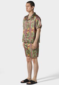 Kurzarmhemd mit Knöpfen und passenden Shorts in einem lebhaften Zitronen- und Blättermuster, das ein rot-grünes gestreiftes Design aufweist.