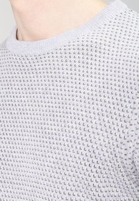 Jasnofioletowy sweter dziergany z fakturą z małymi wypukłymi kropkami, okrągłym dekoltem i ściągaczami przy rękawach. Materiał wydaje się miękki i przewiewny.