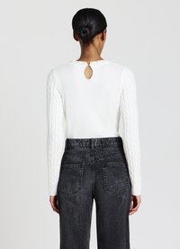 Maglione bianco con maniche a treccia, caratterizzato da un dettaglio a apertura a chiave sul retro. Abbinato a jeans neri sbiaditi a vita alta con tasche posteriori.