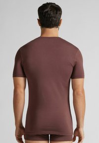 Krótki rękaw, brązowa koszulka bawełniana o dopasowanym kroju, gładkiej fakturze i okrągłym dekolcie; widok z tyłu pokazuje czyste szwy i subtelne detale.