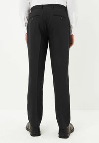 Mustat housut, joissa on räätälöity malli, sisältäen kaksi takataskua ja sileän kangas texture. Yhdistetty kiillotettuihin mustiin kenkiin.