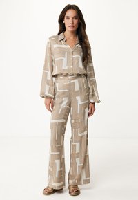 Completo svasato in beige chiaro con motivi geometrici marroni. Camicia con bottoni a maniche lunghe e pantaloni a gamba larga coordinati, realizzati in un tessuto morbido.