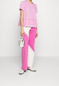 Top rosa de manga corta con estampado geométrico, combinado con pantalones rosa y blanco en bloques de color. Bolsa blanca y zapatos de slip-on.