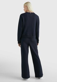 Felpa navy e pantaloni larghi coordinati, realizzati in tessuto morbido con orlo a coste. La vista posteriore mostra un sottile accento rosso al collo.