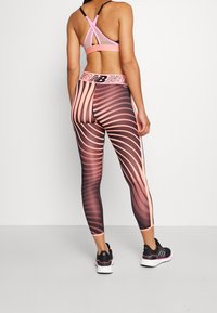 Leggings sportivi con un audace motivo a spirale in nero e pesca, design a vita alta e tessuto elasticizzato. Abbinati a un reggiseno sportivo rosa.