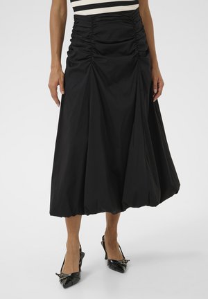 Jupe midi noire en tissu léger, avec des détails froncés à la taille et un bas évasé. Associée à des chaussures noires à talons pointus.