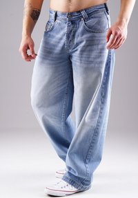 Helle blaue Jeans im relaxed Fit, mit fünf Taschen, sichtbaren Nähten und leichtem Verblassen. Kombiniert mit weißen Sneakers.