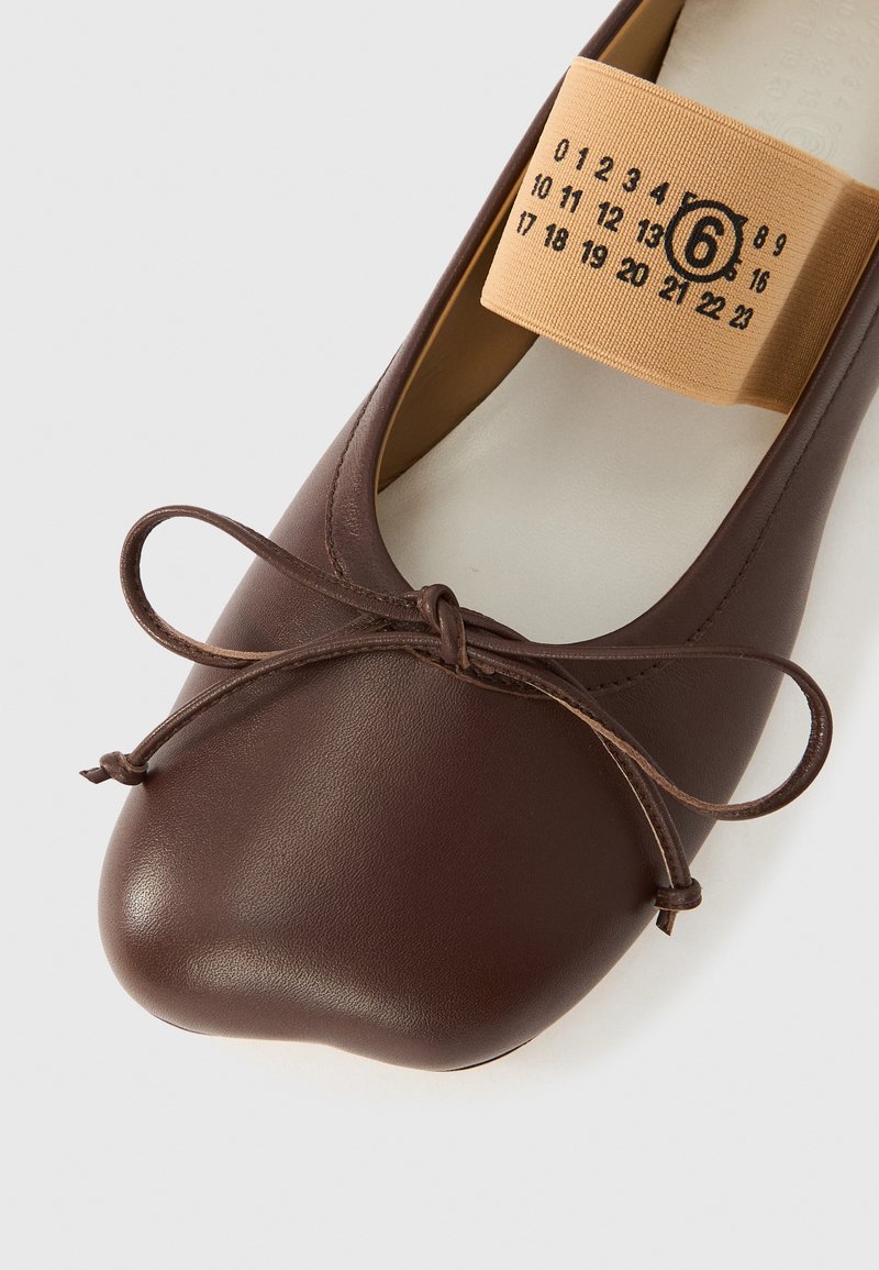 Brun læderballerina med bundet sløjfe på tåen og beige elastikstrop mærket med tal og indrammet størrelse 6.