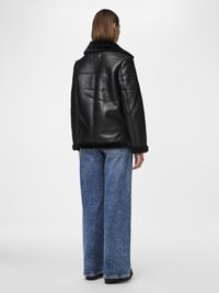 Black leather jacket with a fur-lined collar, rectangular design, and relaxed fit, paired with wide-leg blue denim jeans.
