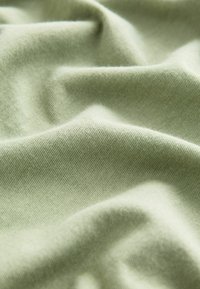 Tissu doux de couleur vert clair avec une texture en maille visible et des plis légers créant des ombres et des reflets subtils.