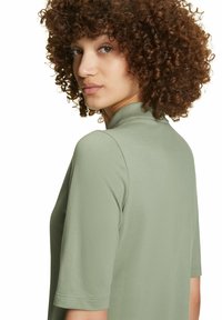 Groene polo met een hoge kraag en korte mouwen. De stof lijkt gestructureerd, met een getailleerde silhouet en een gladde afwerking.