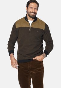 Brown zip-up sweatshirt with a lighter brown shoulder panel, textured fabric, black accents, and a logo on the chest. Paired with brown corduroy pants.