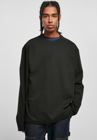 Svart langermet T-skjorte med rund hals og senkede skuldre, laget av et mykt, teksturert stoff; brukt over en blå crew neck-skjorte.