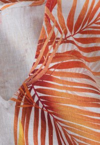 Tissu avec une base blanche ornée de motifs de feuilles de palmier orange et rouge en bold ; texture lisse, léger et tissu tissé avec des coutures visibles.