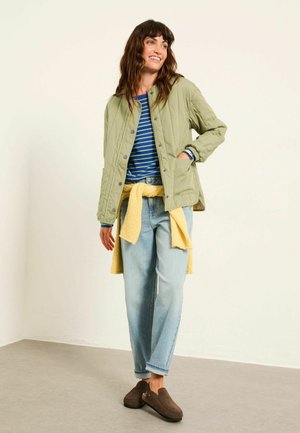 Green quilted jacket with a round collar, navy and white striped shirt, light blue jeans, yellow sweater tied at the waist, brown slip-on shoes.