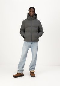 Grå polstret jakke med hætte, med lynlåslukning. Båret over lyseblå jeans og brune støvler med struktureret finish.