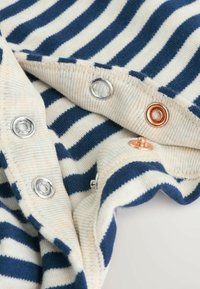 Tessuto a righe in blu navy e crema, con bottoni a pressione in argento e rame, dalla finitura morbida e texturizzata.