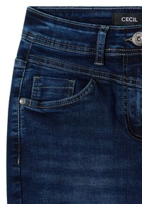 Jean en denim bleu foncé en gros plan montrant la poche avant, la passants de ceinture, le bouton argenté et l'étiquette de marque "CECIL" sur la ceinture.