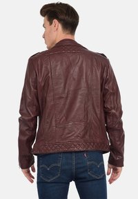 Veste en cuir bordeaux avec un design matelassé sur les épaules et une coupe droite, comportant des poches arrière et une finition lisse.