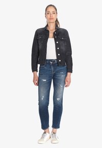 Veste en denim noir avec des boutons sur le devant, deux poches poitrine, jean skinny bleu délavé avec des détails usés, et baskets légères.